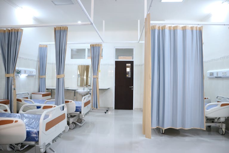 Spacious hospital ward in Surabaya, Indonesia with multiple medical beds and privacy curtains.